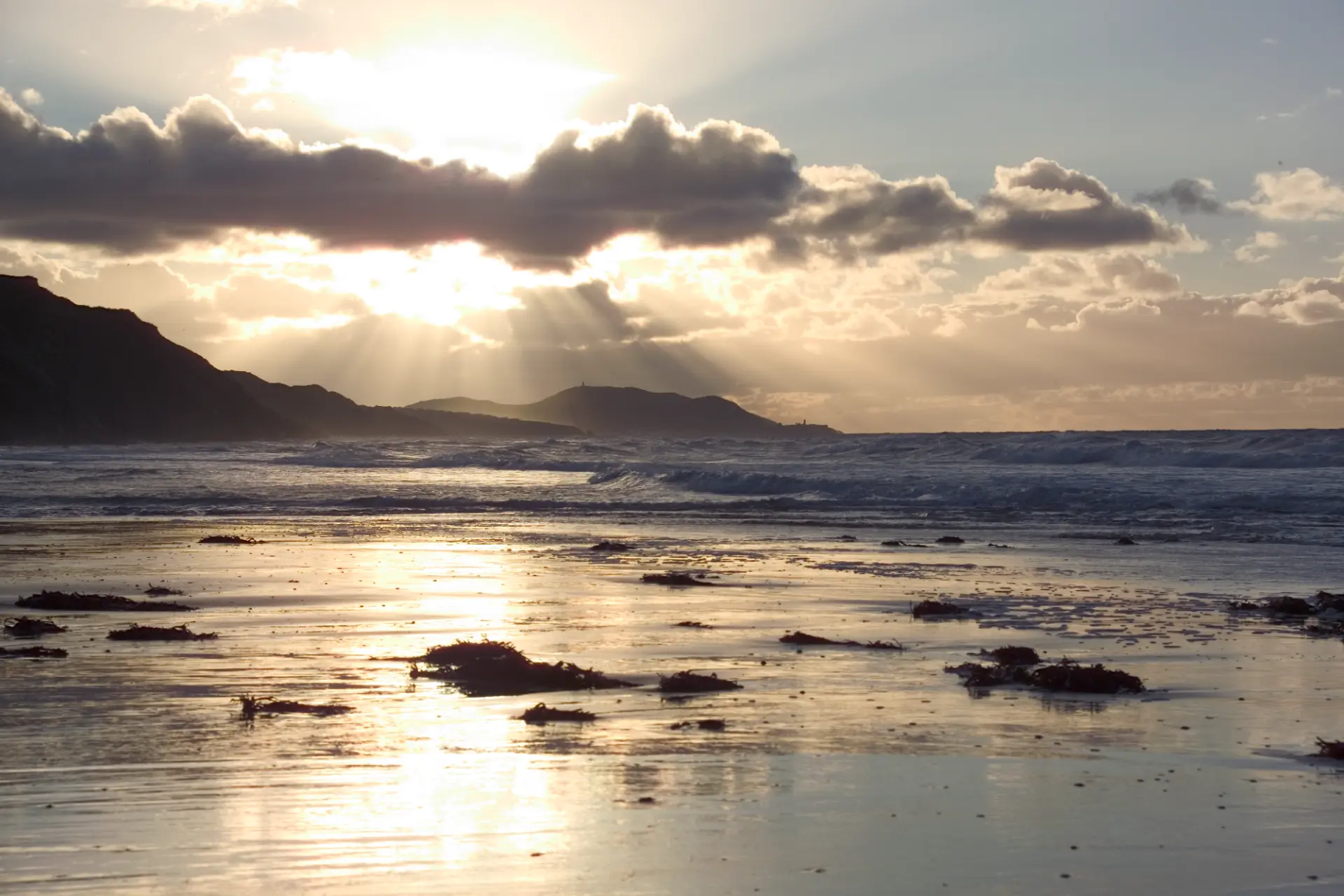 Sunlight breaking through cloud over an Isle of Man beach at low tide